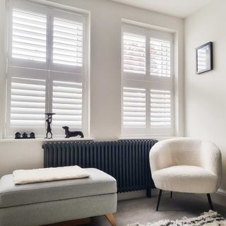 white living room with grey column radiator and cream boucle armchair and wooden white window shutters