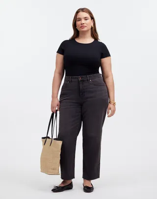 model wears black jeans with a black t-shirt and black flats while carrying a tan raffia tote