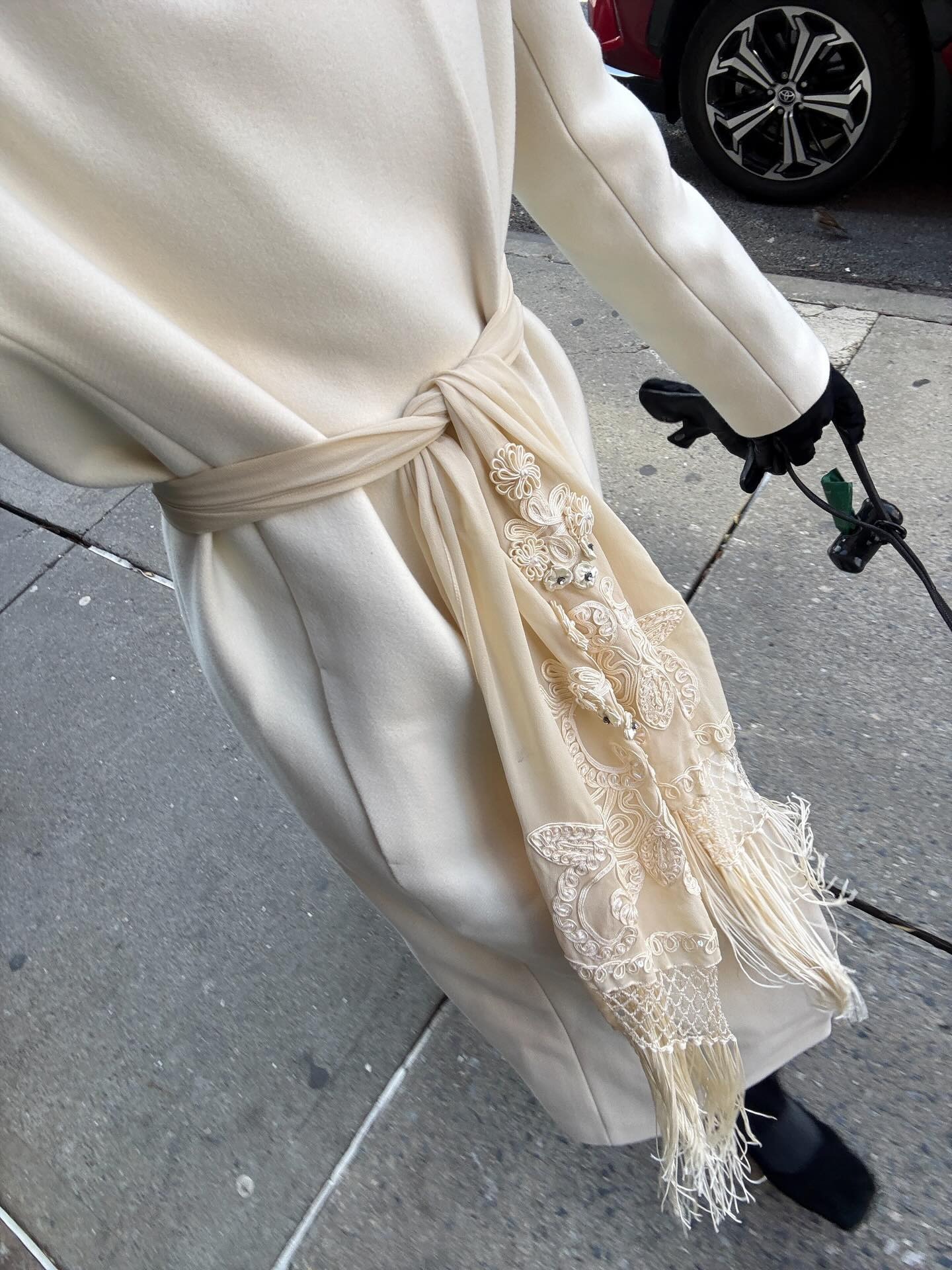 Woman wearing white ivory coat with ivory fringe scarf, black gloves, and black boots.