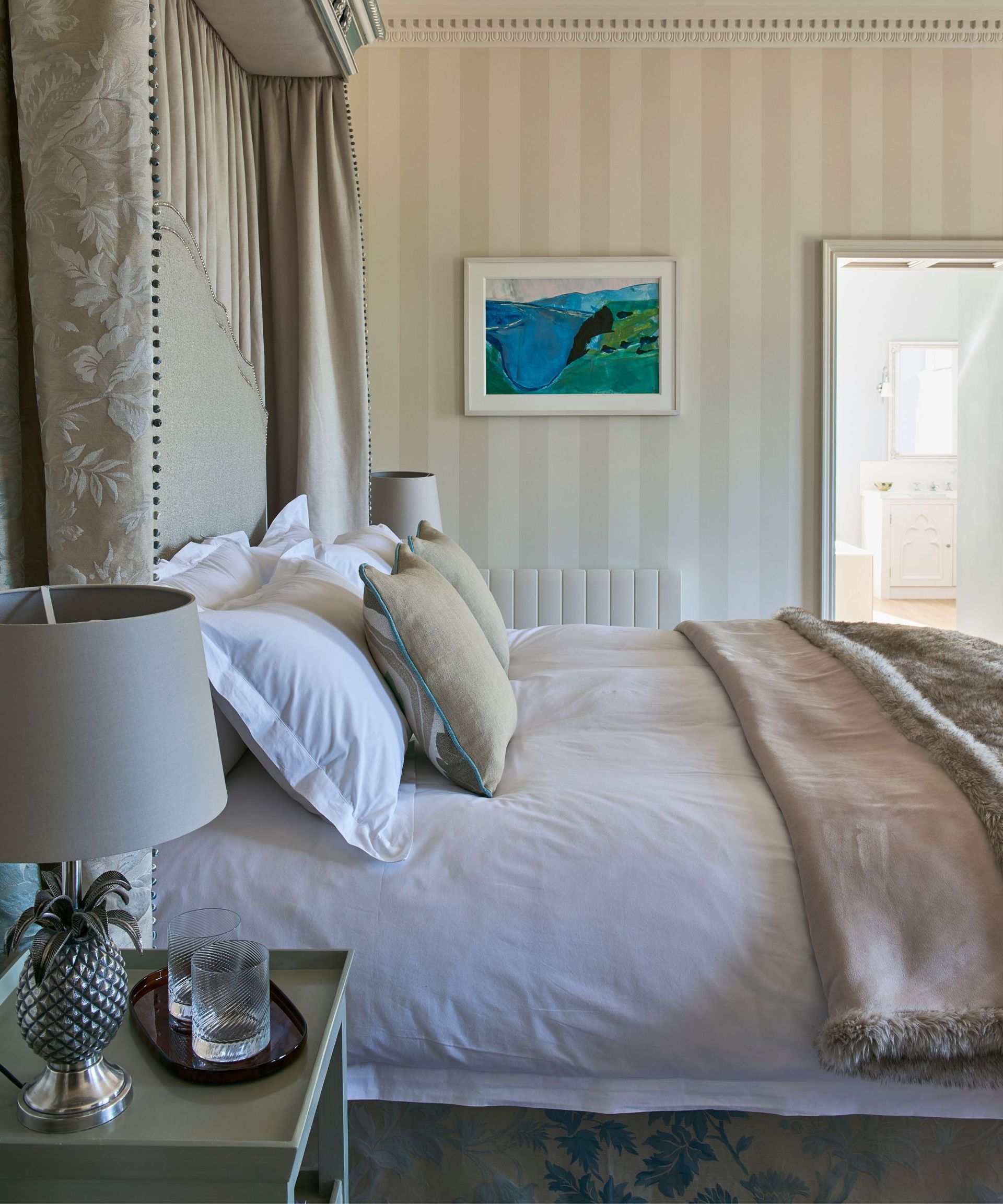 Double bed dressed with neutral coloured bedding, pelmet and curtains round the headboard.