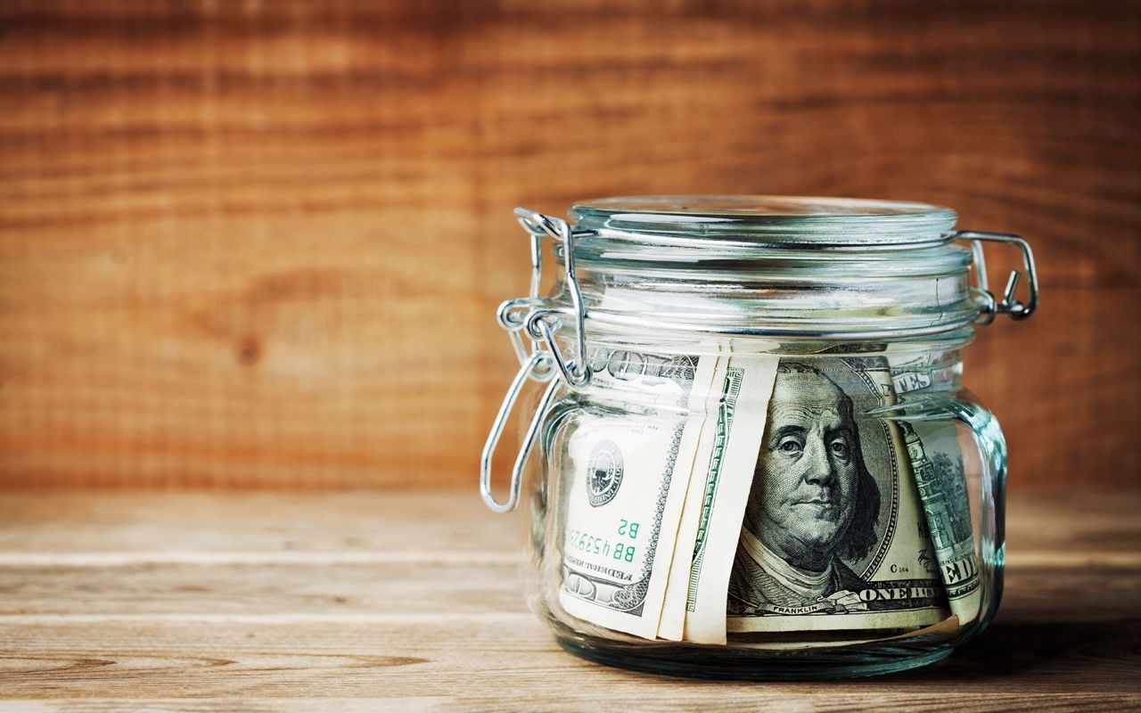 Dollar bills in glass jar on rustic table. Saving money concept.