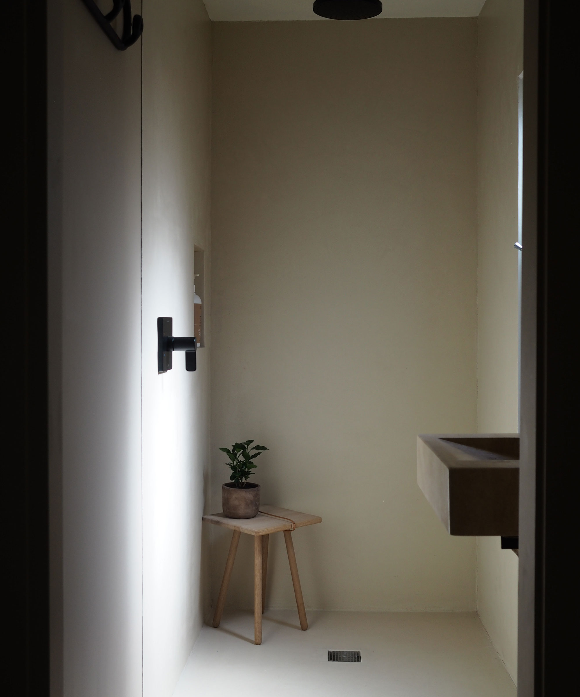 Concrete finish shower with black fixtures and wooden stool with plant in corner