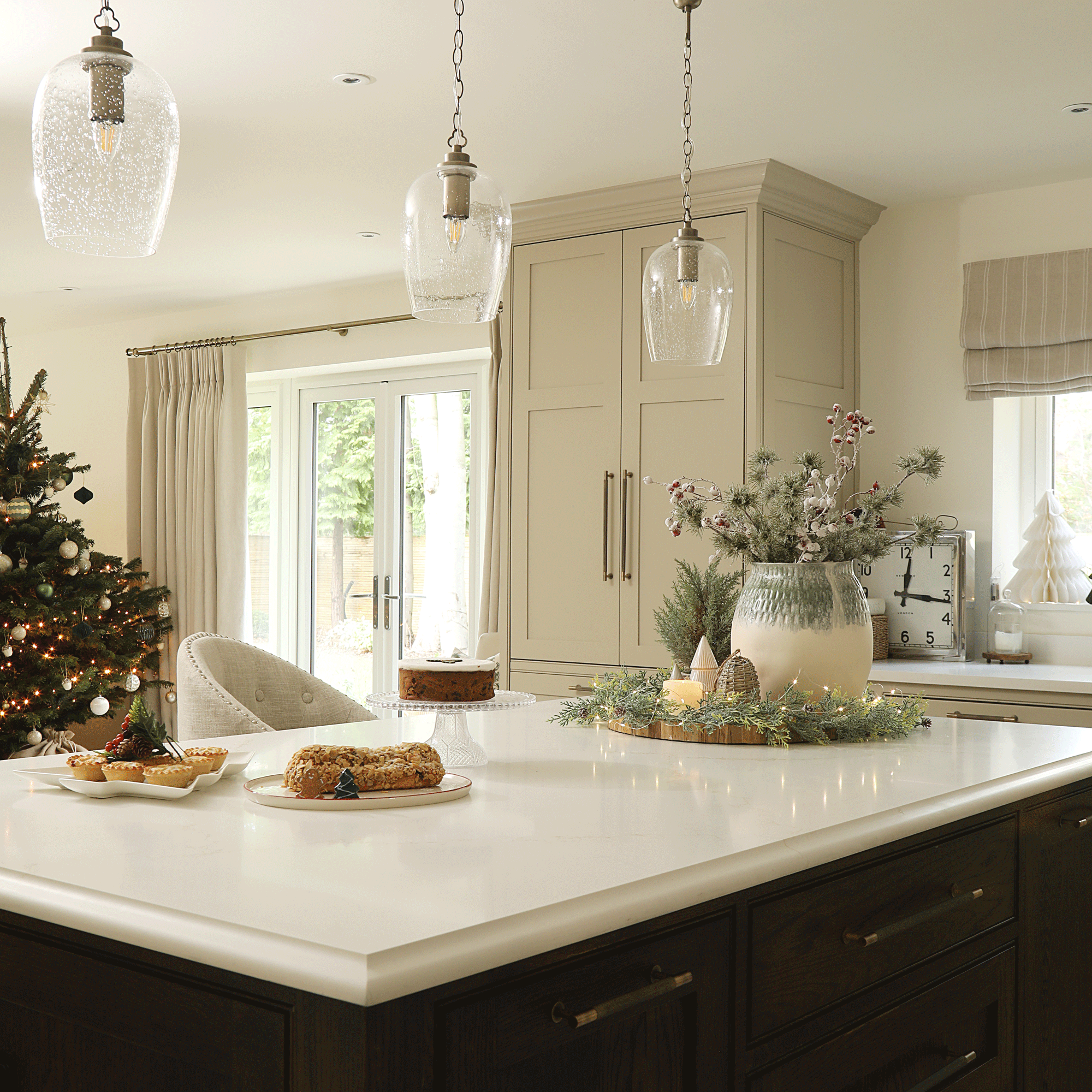 an open plan kitchen with a large kitchen island with three pendants overhead and a Christmas tree