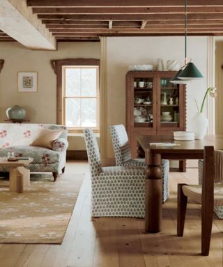 dining room and sofa from the curated cottage anthropologie collection with rustic beams and a farmhouse style dining table and slipcovered chairs