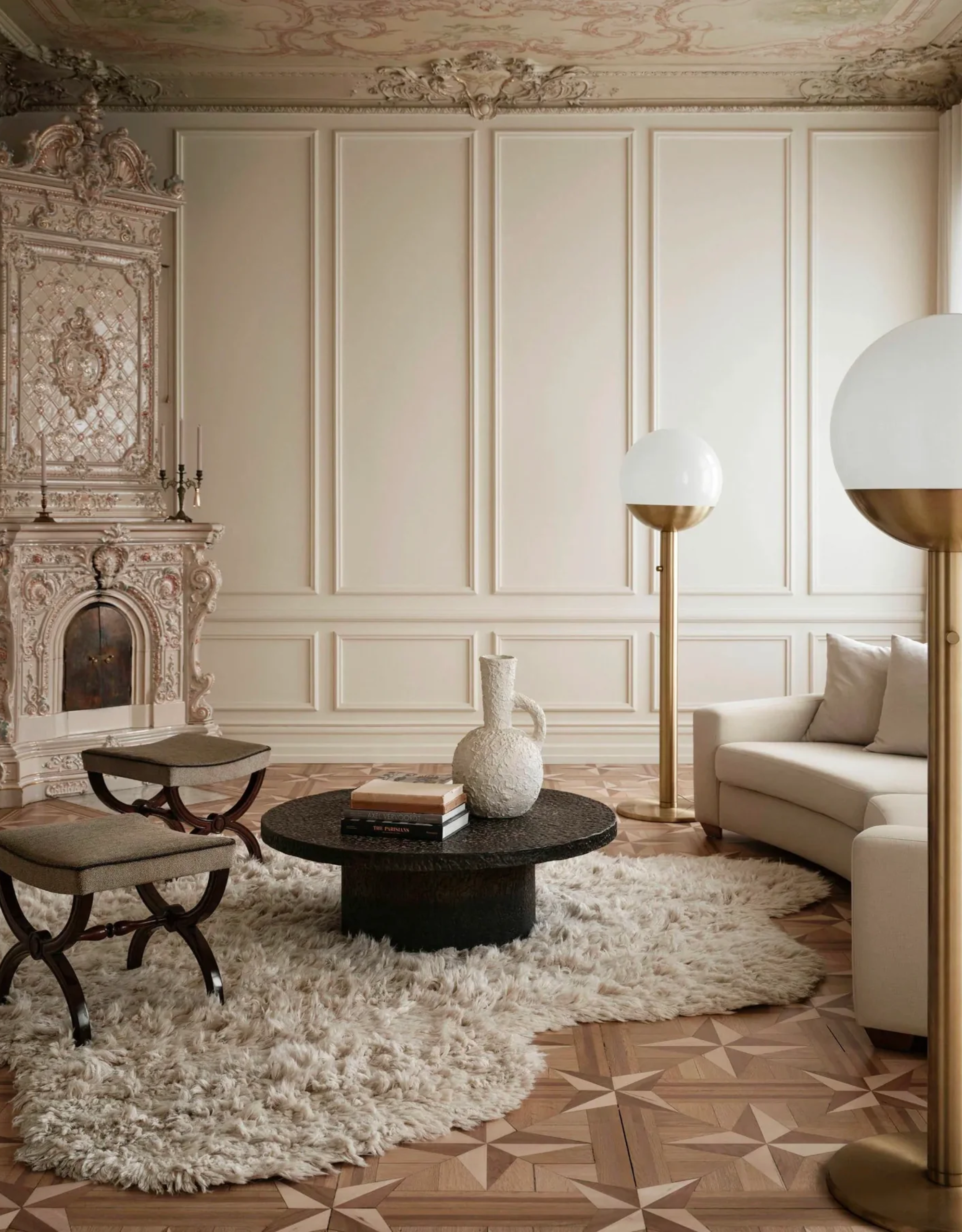 A living room with an ornate fireplace, wall trim, a patterned ceiling, spherical floor lamps, a pair of stools, a shaggy rug, a round low coffee table, a textured vase, and two-toned wood floors