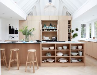 Kitchen island ideas with open storage in pale wood in a white kitchen with high vaulted ceilings.