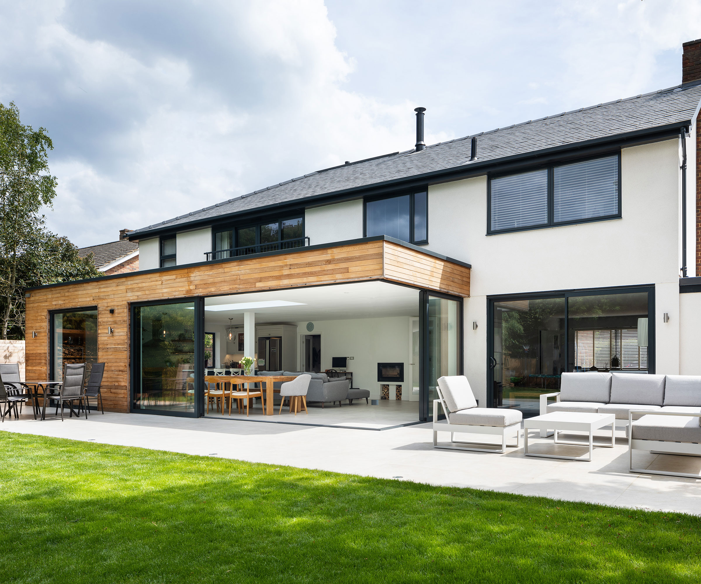 extended house with a timber-clad extension featuring corner sliding doors that completely open up the new space to the patio and garden
