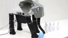 A photograph of a robot elephant with a ball standing next to bowling pins. 