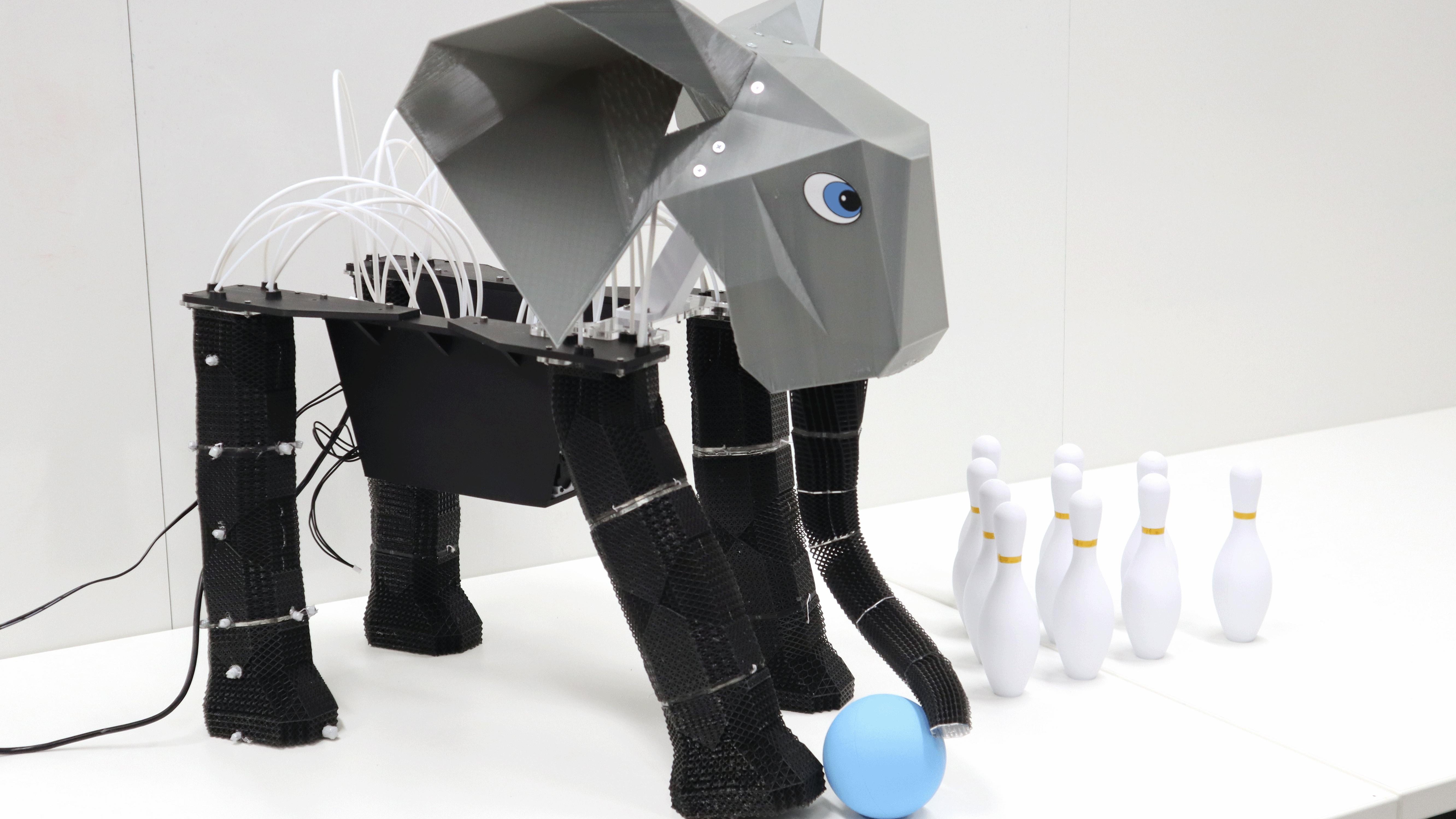 A photograph of a robot elephant with a ball standing next to bowling pins. 