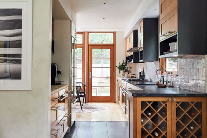 wooden kitchen units with black countertops and wine store with door to garden in background