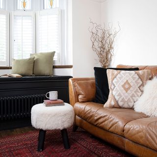 White living room with tan leather sofa, bay window with window seat, boucle stool, Ikat cushion