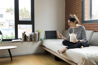 Woman eating takeaway food and researching why can't I lose weight on phone, sitting on sofa