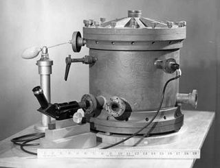 Black and white image of a cylindrical apparatus with a viewing scope in front of a ruler