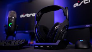 An Astro Gaming headset on a desk alongside two monitors, a keyboard and a microphone.