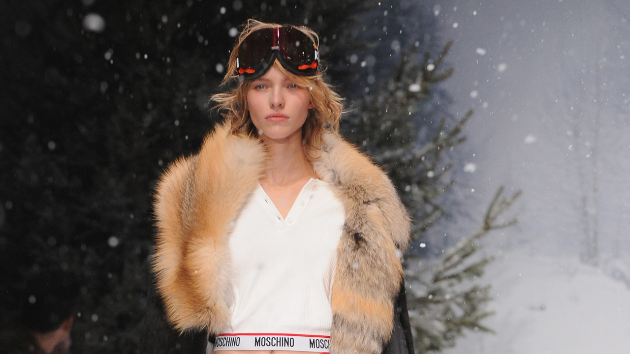 model walks down the catwalk with fake snow wearing a fur coat and ski goggles - Skiing skincare routine