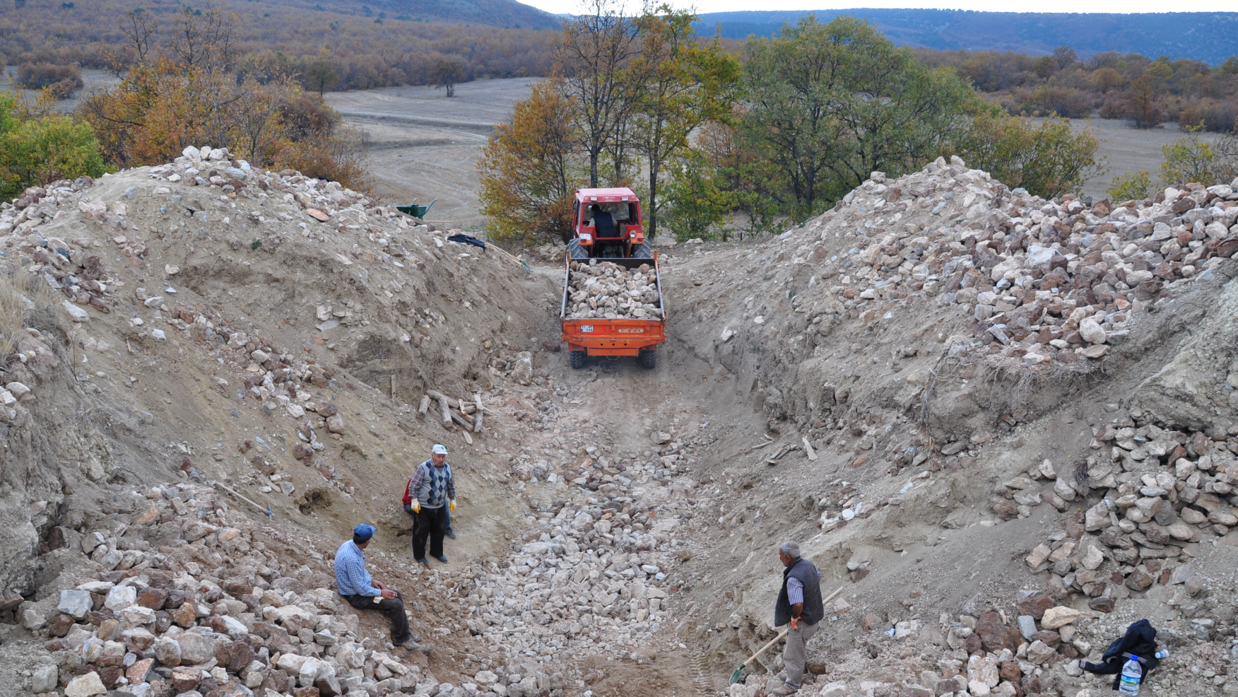 archaeologists stand in a rocky trench with a bulldozer