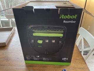 The Roomba s9+ in its box on a wooden table