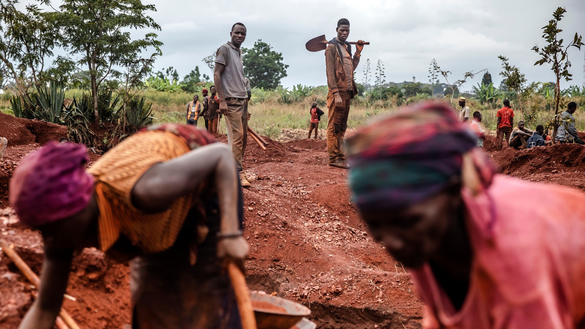 Two gold miners watch as women miners work at an open-pit gold mine in Nyarugusu, Tanzania 
