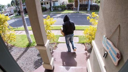 Staged photo of a 'porch pirate' stealing a package from a residence's front door, as captured by a video doorbell.