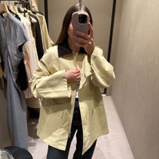 Woman takes photo in changing room wearing country jacket. 