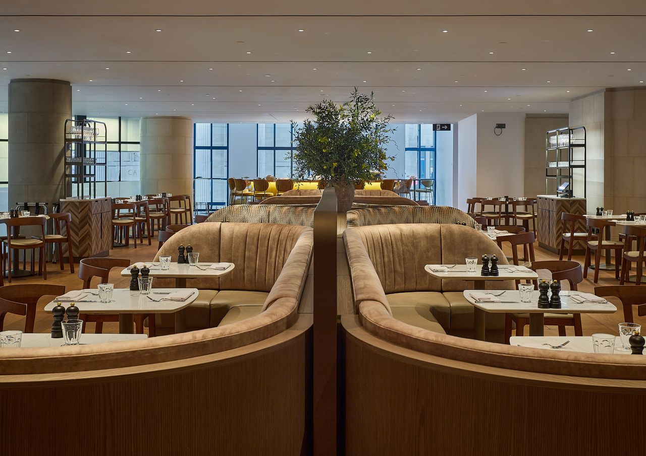 The interiors of a retro-inspired restaurant feature sinuous lines, textured upholstery, and tactile wooden furniture, along with a dazzling, bronze cocktail bar.