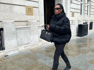 Fashion influencer @nlmarilyn in London wearing an all-black winter outfit with black knee-high riding boots, black leggings, a black puffer jacket, and black accessories.