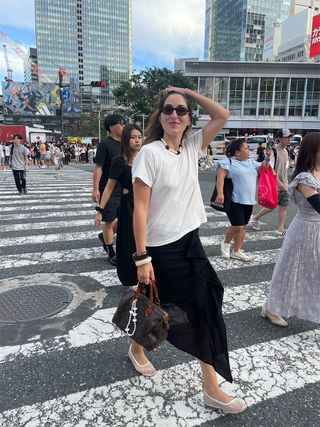 Anna LaPlaca trägt in Tokio ein weißes Naadam-T-Shirt mit einem schwarzen Midirock und weißen Mesh-Flats