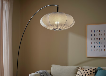 An arched floor lamp with a light blue textile shade overhanging a sofa