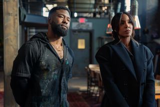 a man (trevante rhodes) wearing paint-splattered overalls and a woman (kelly rowland) wearing a coat stand in a loft in a still from mea culpa