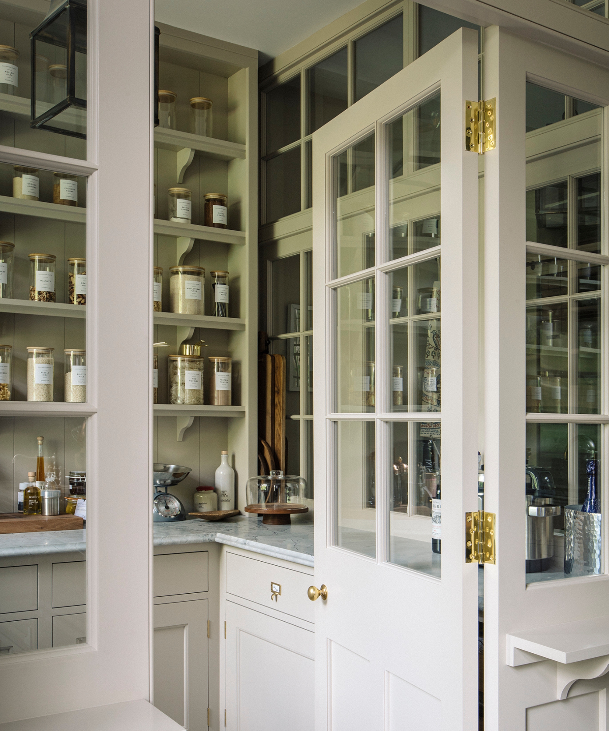 A small walk-in pantry with glazed doors and cream cabinets