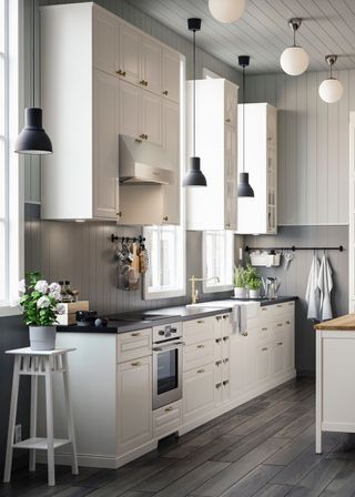 a white kitchen with cabinets and drawers. There are pendant lights hanging above the worktops and stove. Beside the kitchen counter is a stool with flowers on top.