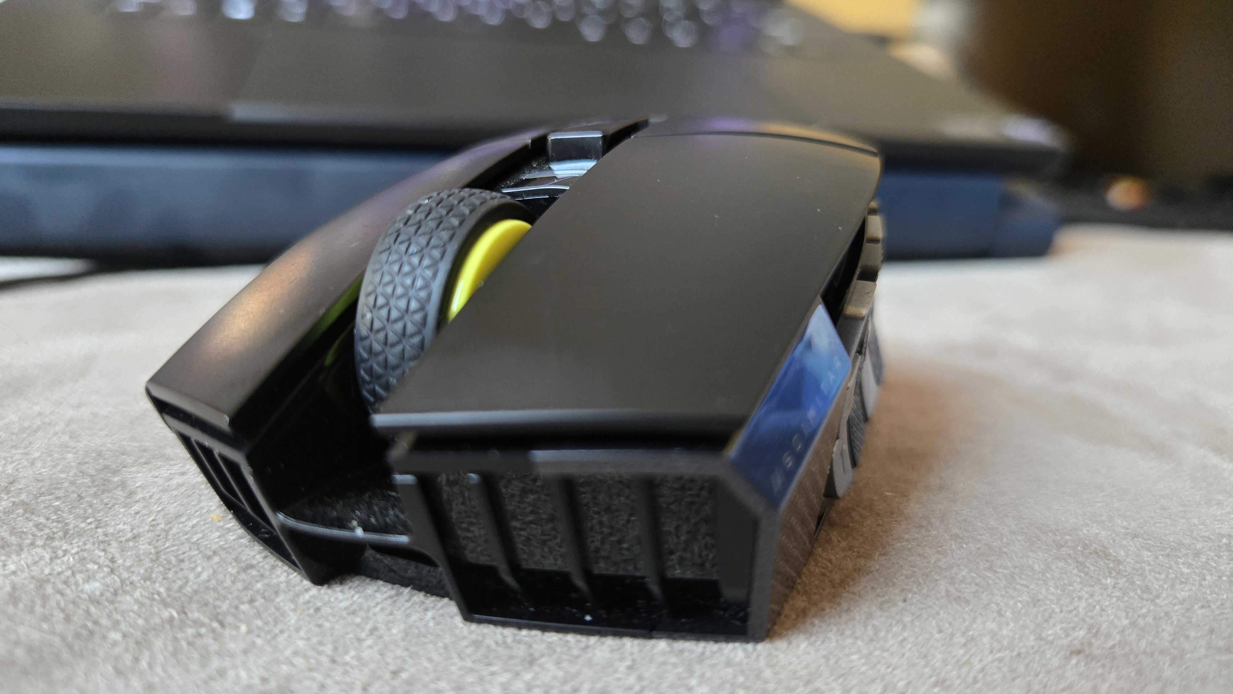 A Corsair Scimitar Elite Wireless SE gaming mouse on a carpet next to a gaming laptop and Stream Deck.