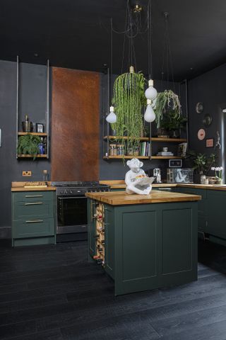 Green Shaker-style kitchen with wood worktops, copper splashback, pendant lights and black floorboards
