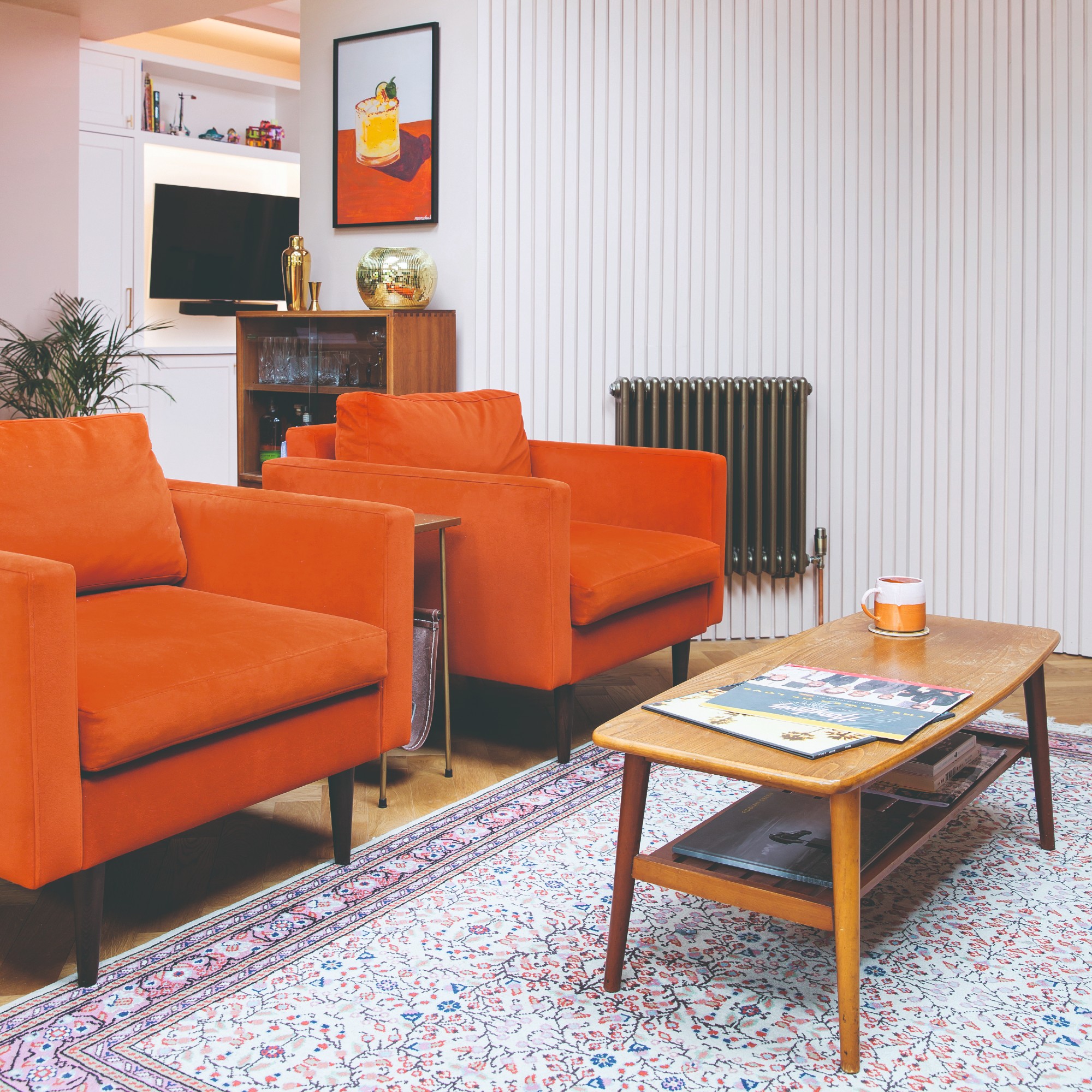 A panelled living room with two orange armchairs in place of a sofa and a midcentury modern coffee table