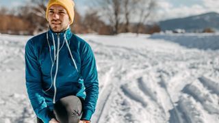 A man stops to stretch while running in the snow