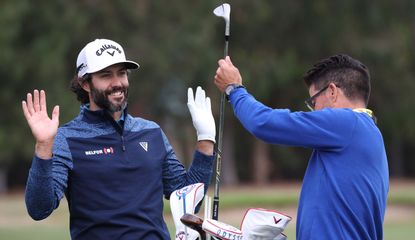 Hadwin raises his hands whilst his caddie puts the club in the bag