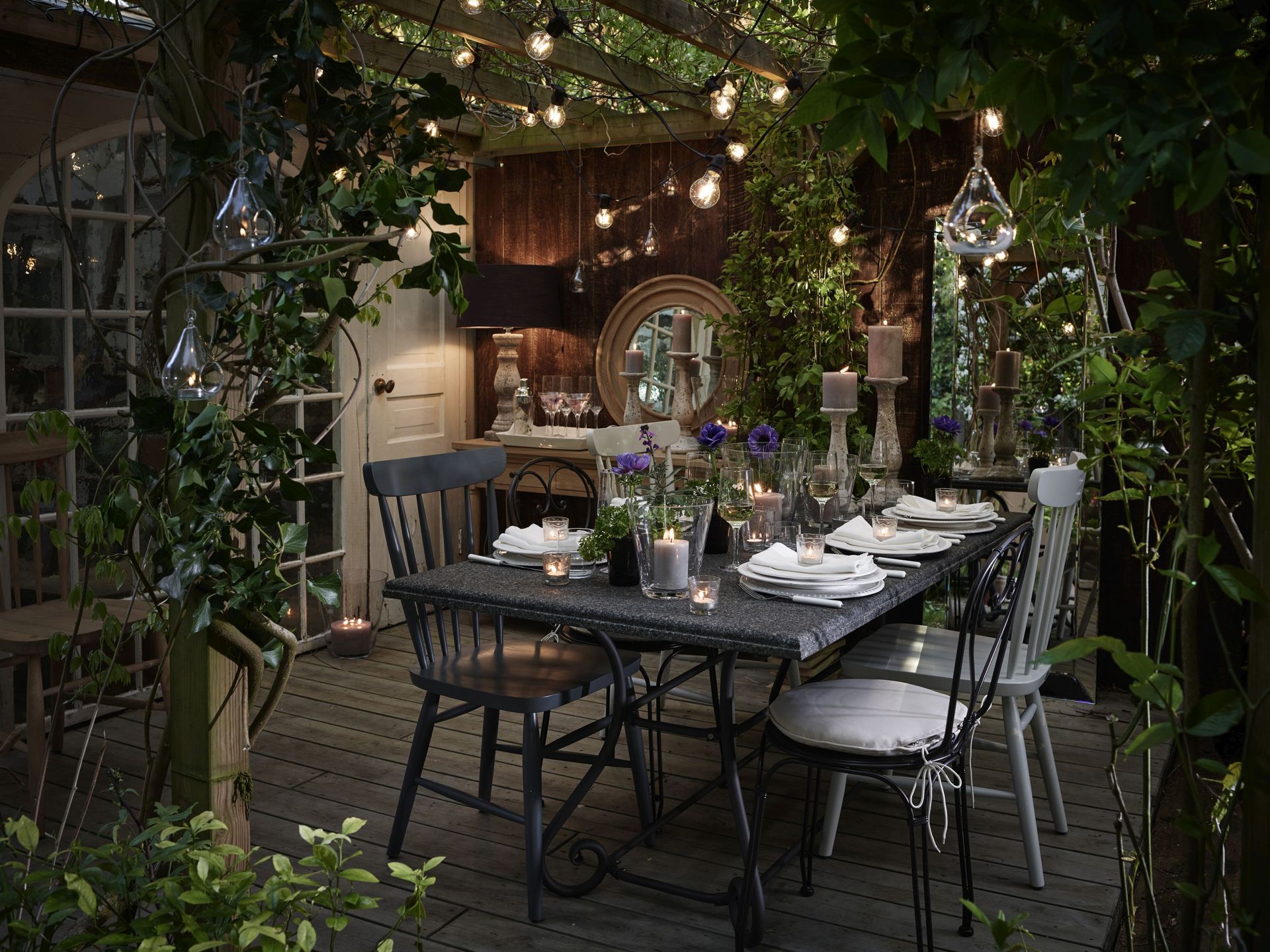 Outdoor dining table lit up by fairy lights draped over pergola