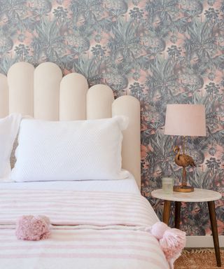 A bedroom with pink and green wallpaper, a white bed with a pink throw, and a pink and bronze lamp
