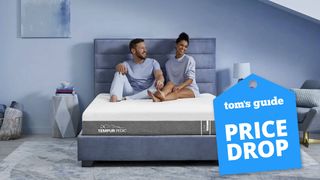 Best tempur-pedic mattress deals and sales image features a couple sitting on the Tempur-Cloud mattress, with a blue 'price drop' badge overlaid on the image