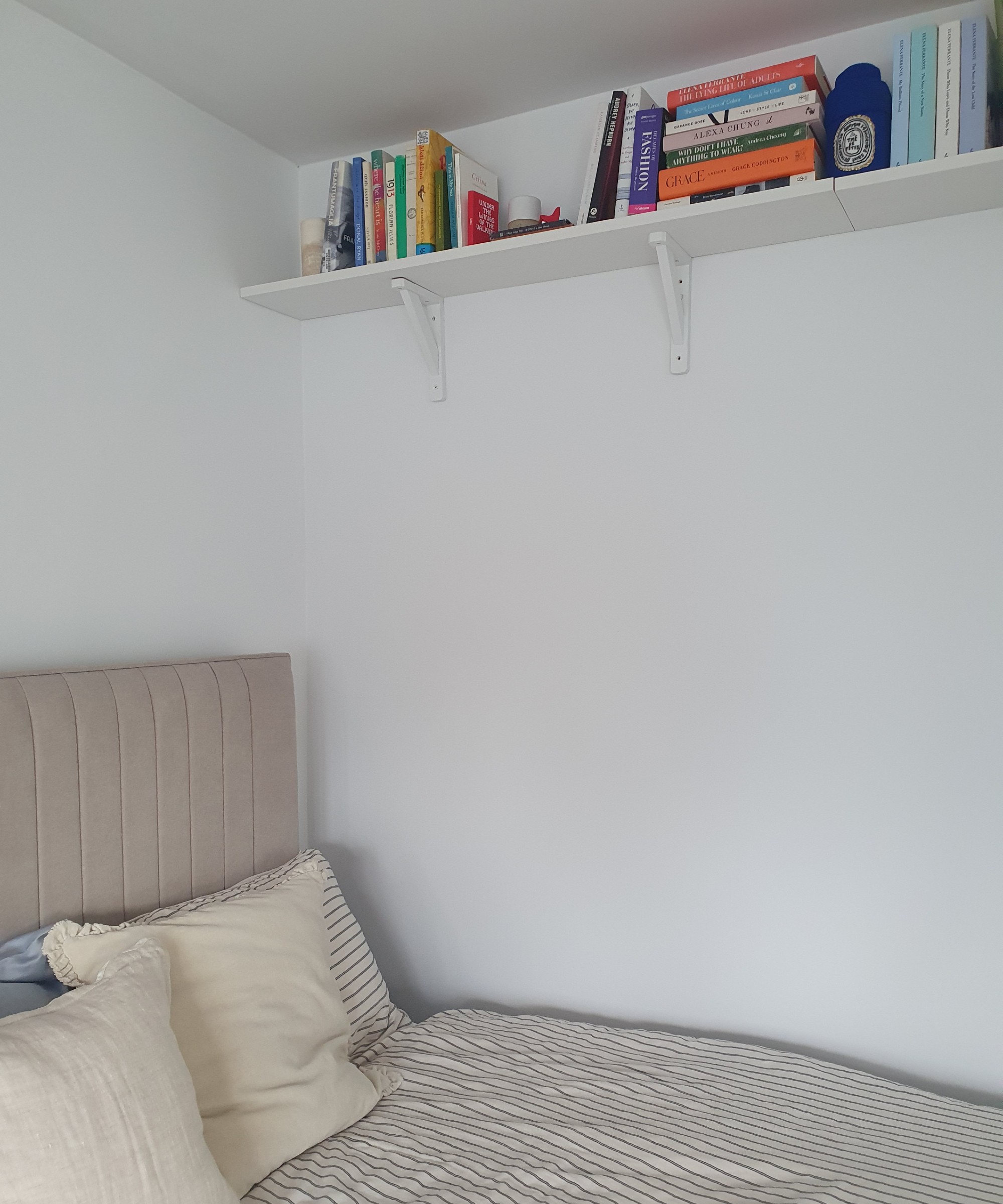 A bed with striped bed linen set against white walls with a wall shelf near the ceiling displaying books