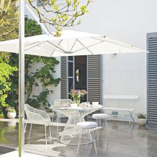 A patio with a white metal dining set and a large white parasol
