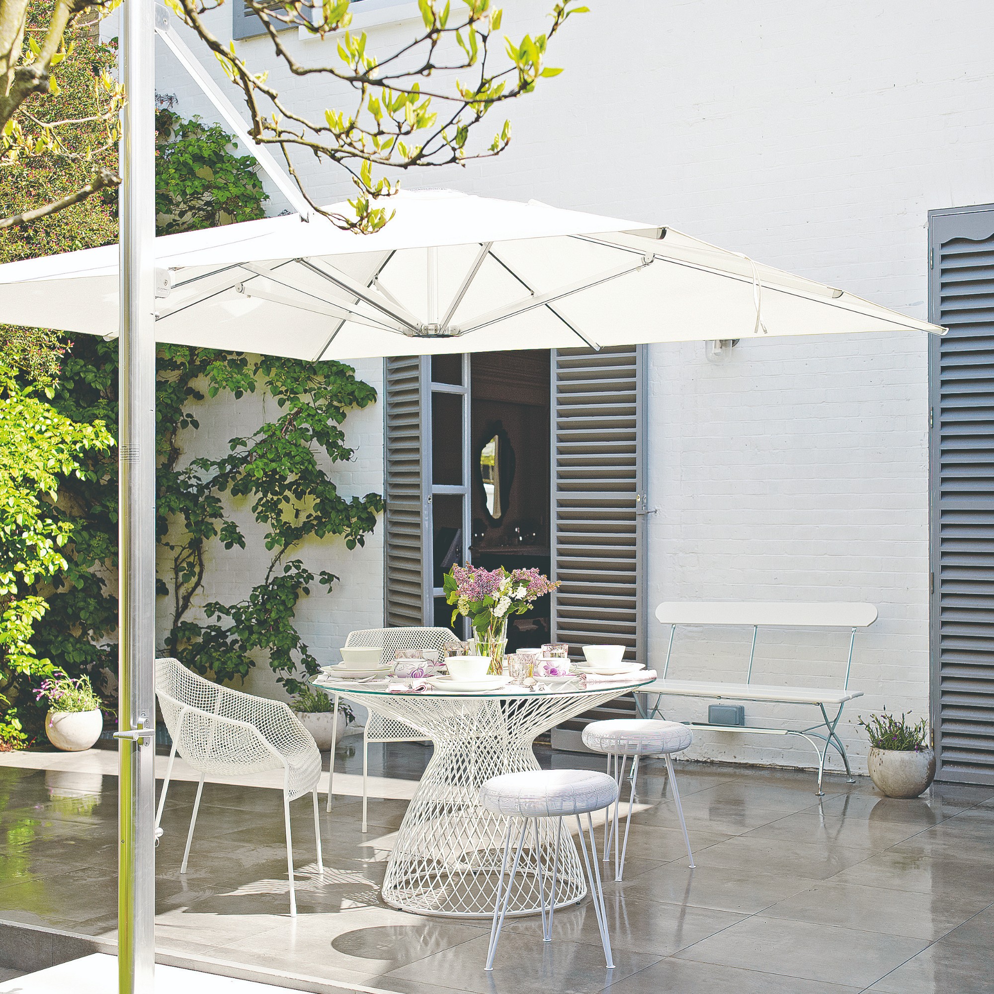 A patio with a white metal dining set and a large white parasol