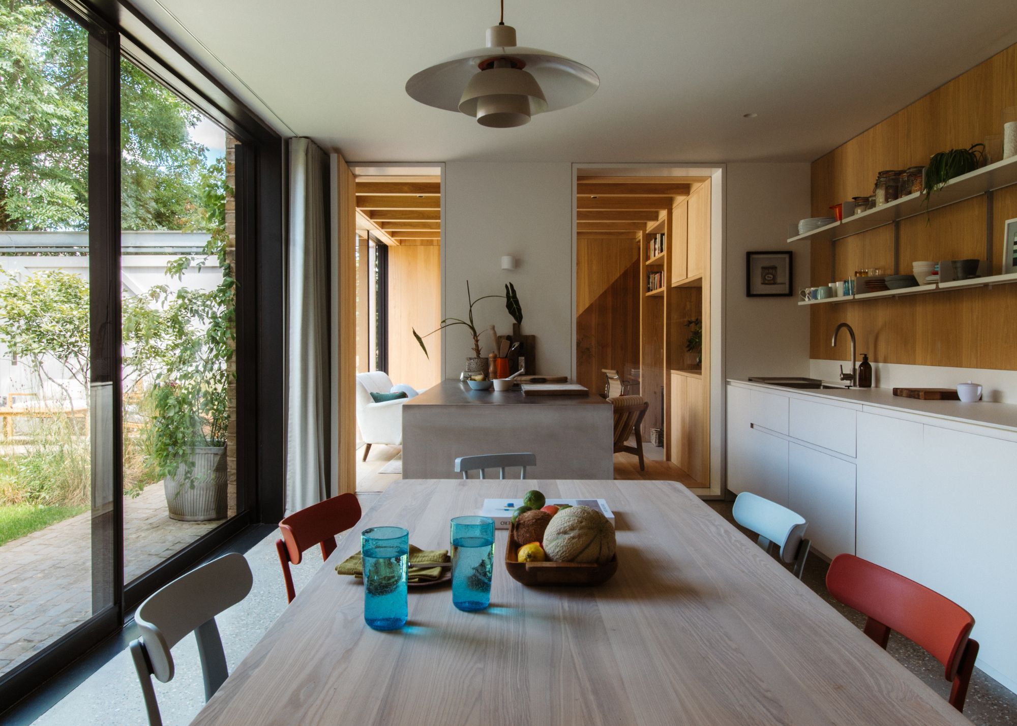 modern kitchen with white walls and cabinets, large wooden table and colorful chairs with sliding glass doors leading to the garden