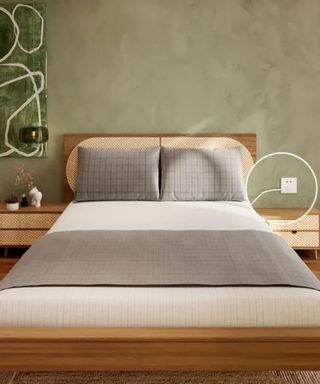 Gray and cream grounding sheets on a wooden bed frame against a green wall.