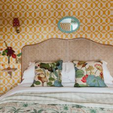 Yellow bedroom with rattan headboard, floating bedside tables and wall mounted lamps