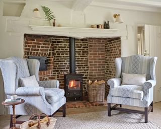 brick inglenook fireplace in an old cottage with armchairs uplholstered in white and blue fabric