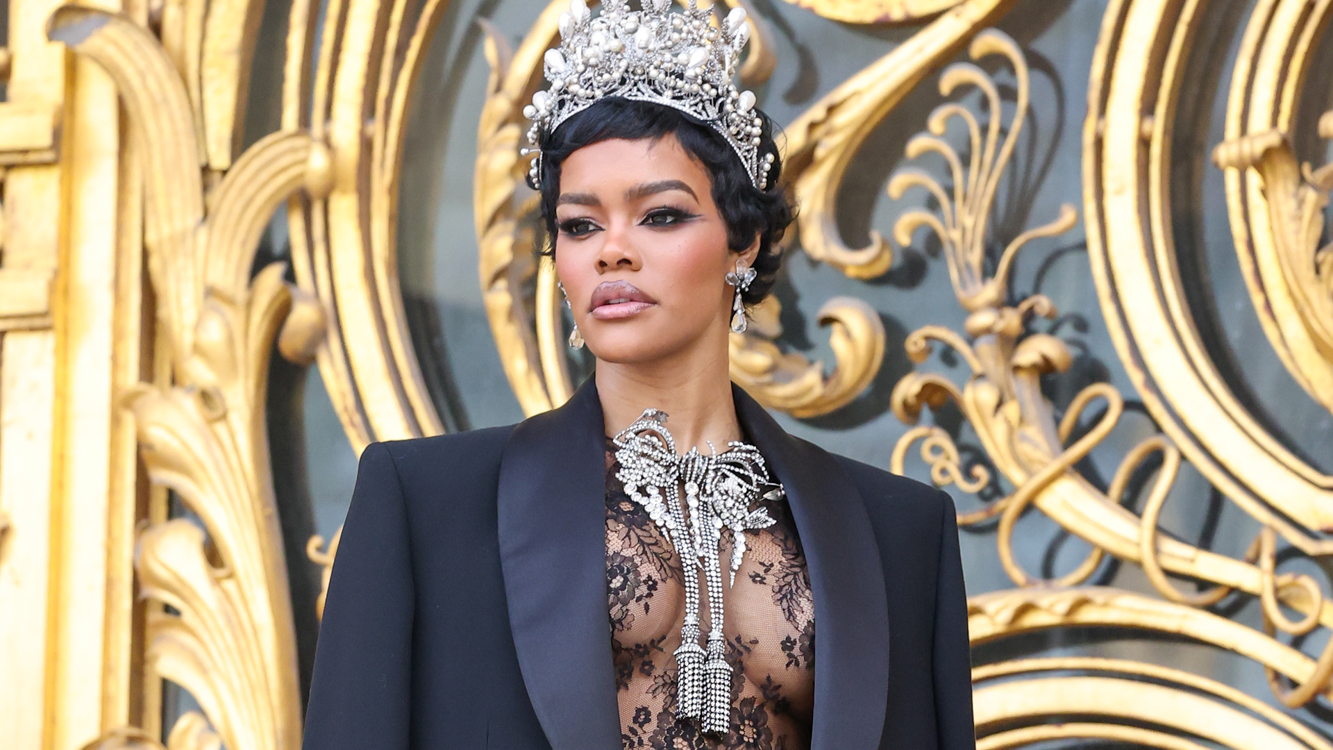 Teyana Taylor arrived at the Schiaparelli couture show in a lace little black dress, a crown, and a bow necklace inspired by her golden globes back