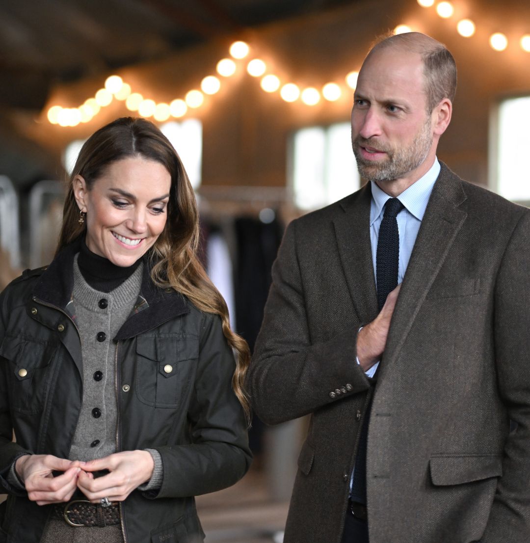 Prince William and Princess Kate wearing brown outfits standing in front of white lights