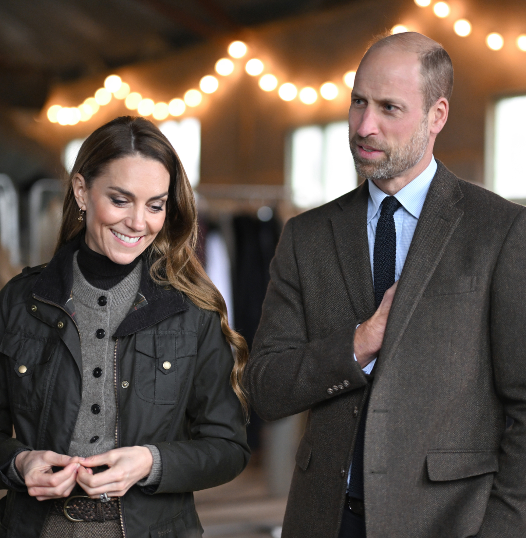 Prince William and Princess Kate wearing brown outfits standing in front of white lights