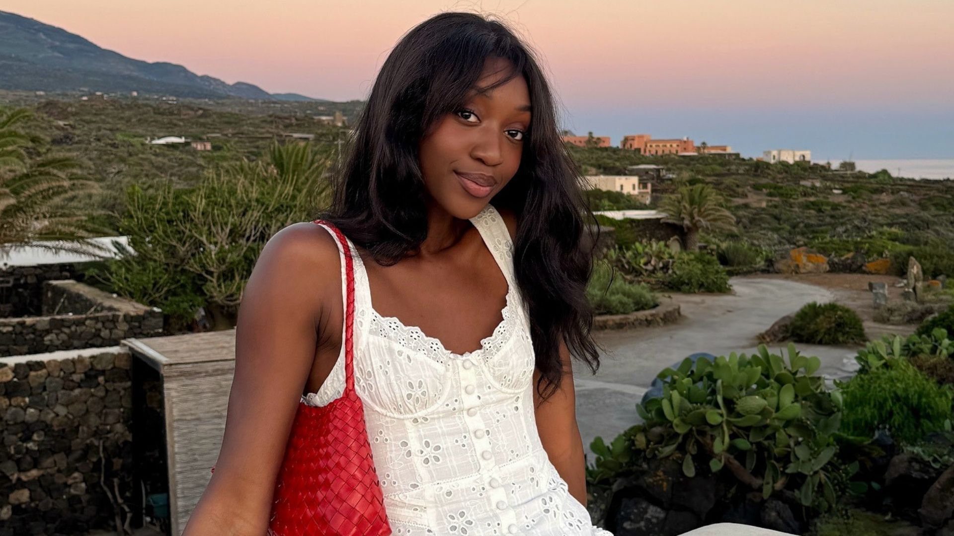 Influencer @emmanuellek_ wears a white mini broderie dress with a red woven shoulder bag.